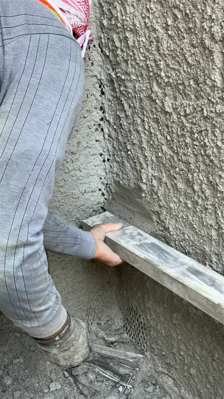 A plasterer ruling cement plaster straight with an aluminium straightedge