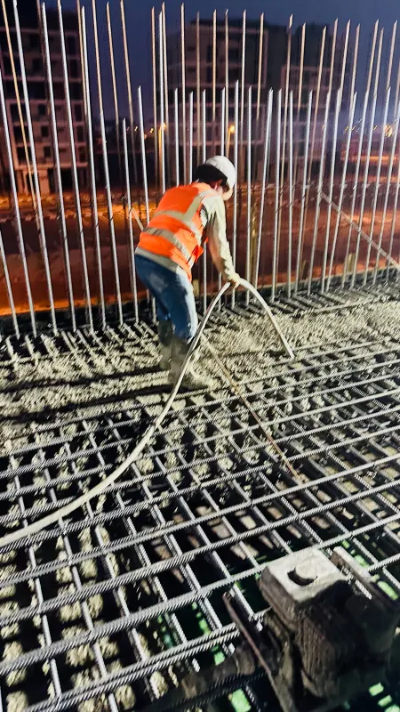 A worker placing concrete across the slab reinforcement at dusk