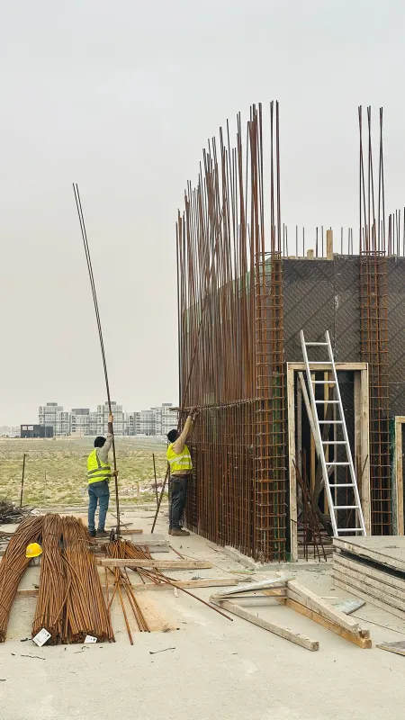 Two steel fixers tying the reinforcement cages of the concrete walls, a ladder against the formwork